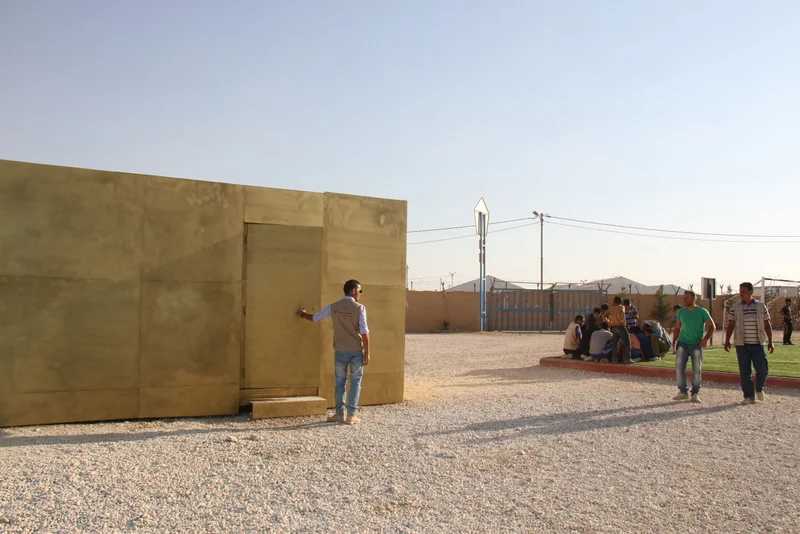 A gold Portal installation in a refugee camp, children gathered at the entrance